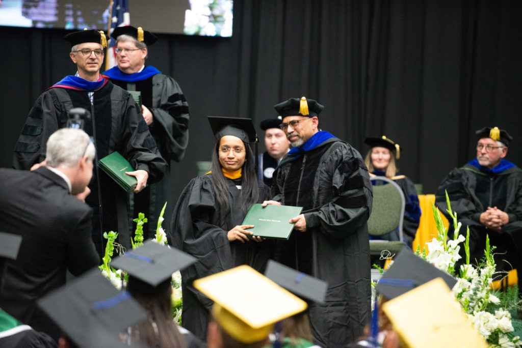 A student receiving their diploma cover from the College of Business's Dean